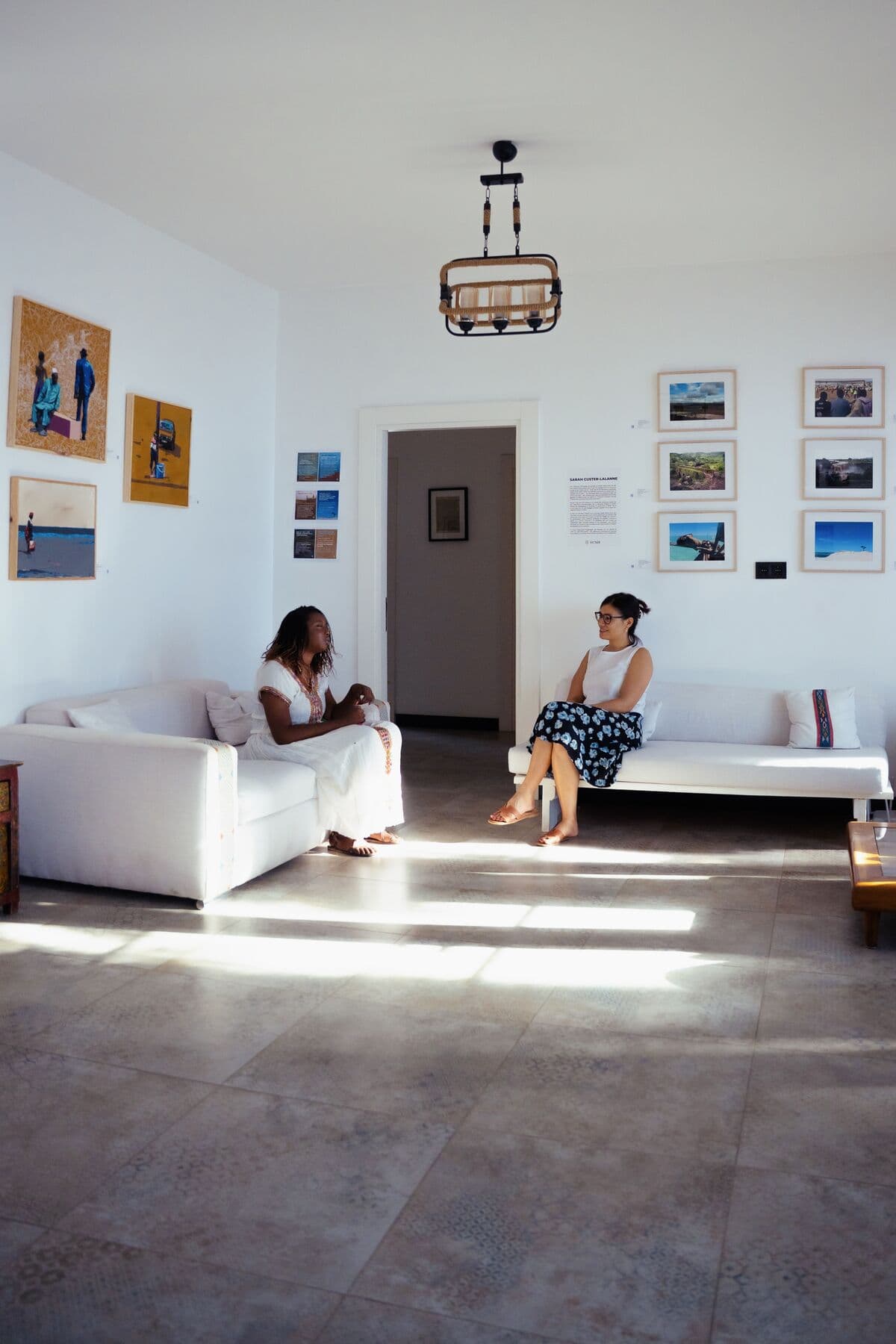 Deux visiteuses dans le salon galerie, entre canapés blancs et œuvres au mur