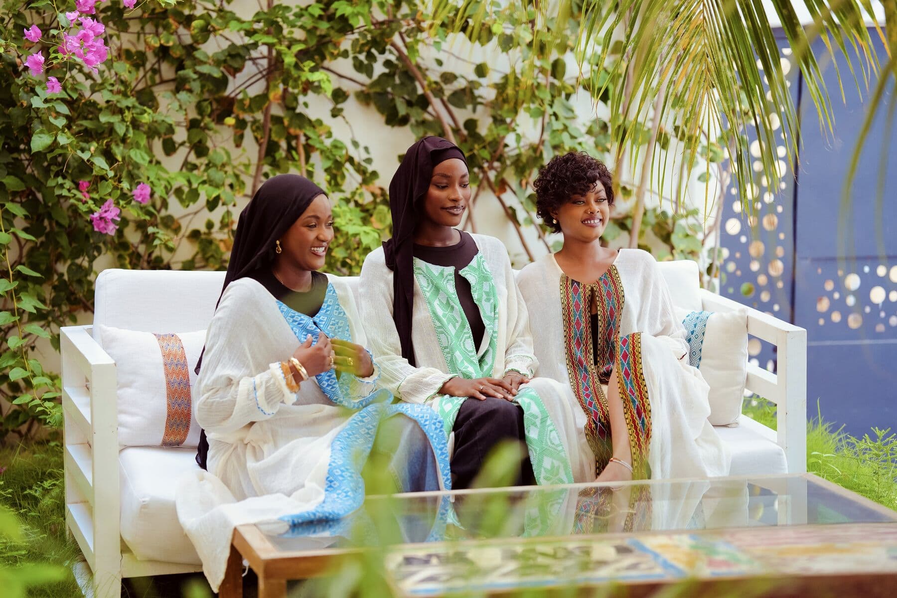 Trois femmes en kaftans blancs brodés, assises au jardin